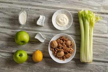 Ingredients for making Waldorf salad with celery, apples and walnuts on a light wooden background in rustic style