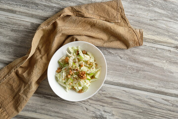 Waldorf salad with celery, apples and walnuts on a light wooden background in rustic style