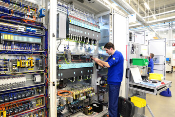 young apprentice assembles components and cables in a factory in a switch cabinet - workplace...