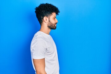 Young arab man with beard wearing casual white t shirt looking to side, relax profile pose with natural face and confident smile.