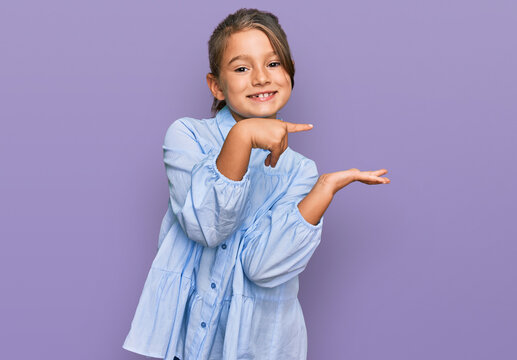 Little beautiful girl wearing casual clothes amazed and smiling to the camera while presenting with hand and pointing with finger.