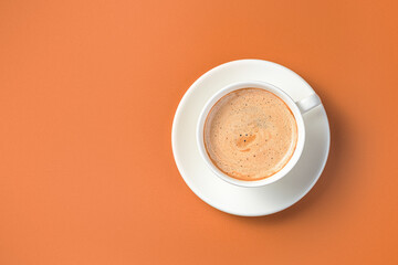 Coffee in a white cup and saucer on a terracotta background. Morning cappuccino.