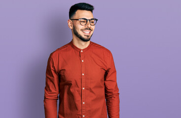 Young hispanic man with beard wearing business shirt and glasses looking away to side with smile on face, natural expression. laughing confident.