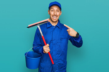 Bald man with beard wearing glass cleaner uniform and squeegee smiling happy pointing with hand and...
