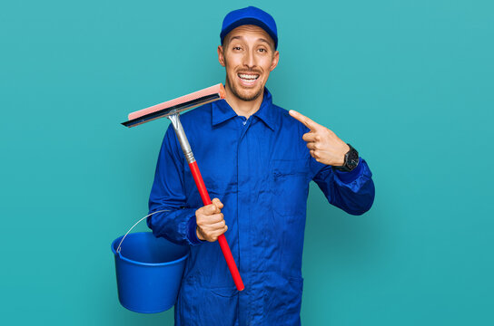 Bald man with beard wearing glass cleaner uniform and squeegee smiling happy pointing with hand and finger