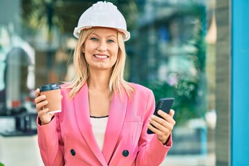 Young caucasian architect woman using smartphone and drinking coffee at the city