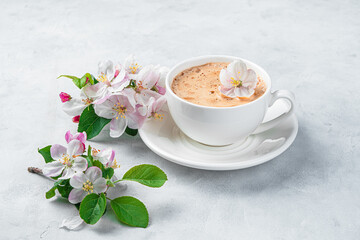 Delicate, beautiful flowers and a cup of cappuccino on a light gray background. Side view.