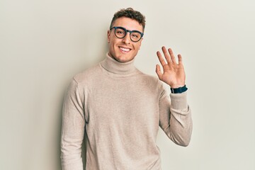 Hispanic young man wearing casual turtleneck sweater waiving saying hello happy and smiling, friendly welcome gesture