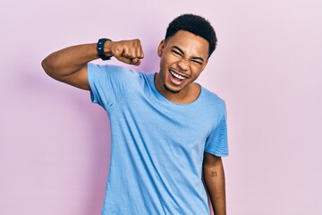 Young african american man wearing casual blue t shirt angry and mad raising fist frustrated and furious while shouting with anger. rage and aggressive concept.