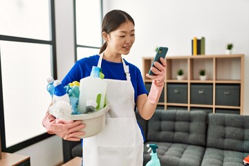 Young chinese housewife holding cleaning products using smartphone at home. © Krakenimages.com