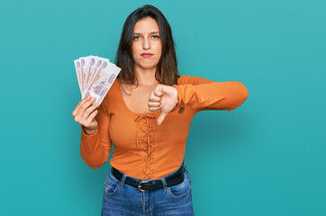 Beautiful hispanic woman holding russian 500 ruble banknotes with angry face, negative sign showing...