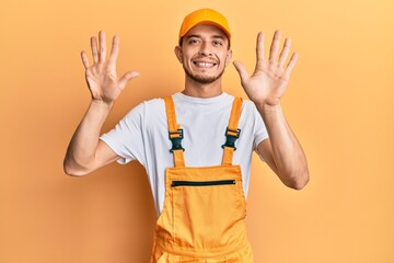 Hispanic young man wearing handyman uniform showing and pointing up with fingers number ten while smiling confident and happy.