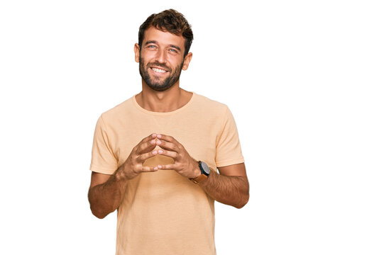Handsome young man with beard wearing casual tshirt hands together and fingers crossed smiling relaxed and cheerful. success and optimistic