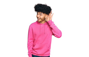 Young african american man with afro hair wearing casual pink sweatshirt smiling with hand over ear listening an hearing to rumor or gossip. deafness concept.