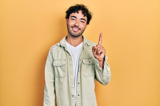 Young hispanic man wearing casual clothes showing and pointing up with finger number one while smiling confident and happy.