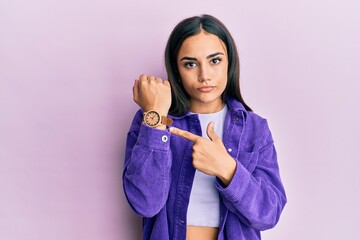 Young brunette woman wearing casual clothes in hurry pointing to watch time, impatience, looking at...