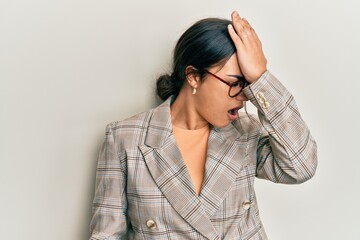 Young brunette woman wearing business jacket and glasses surprised with hand on head for mistake,...