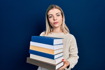 Beautiful caucasian woman holding a pile of books relaxed with serious expression on face. simple and natural looking at the camera.