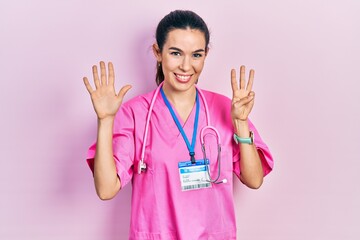 Young brunette woman wearing doctor uniform and stethoscope showing and pointing up with fingers number eight while smiling confident and happy.