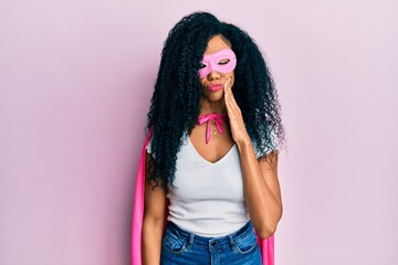 Middle age african american woman wearing super hero costume touching mouth with hand with painful expression because of toothache or dental illness on teeth. dentist