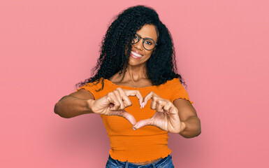 Middle age african american woman wearing casual clothes and glasses smiling in love doing heart symbol shape with hands. romantic concept.