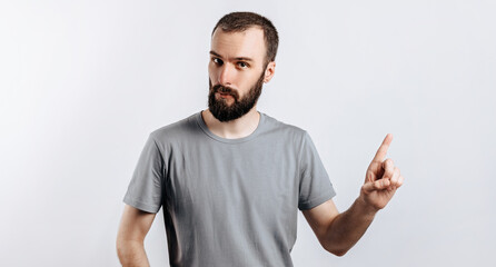 Portrait of cheerful young handsome man smiling looking at camera pointing finger upwards on white background with space for advertising mock up