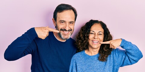 Middle age couple of hispanic woman and man hugging and standing together smiling cheerful showing and pointing with fingers teeth and mouth. dental health concept.