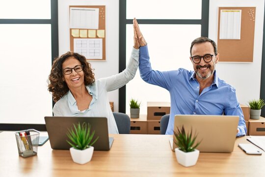Two middle age business workers smiling happy and high five at the office.