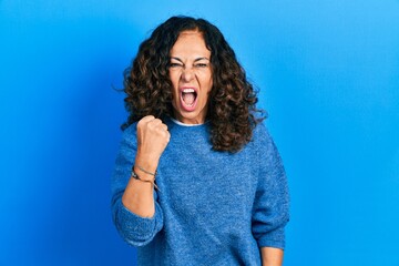 Middle age hispanic woman wearing casual clothes angry and mad raising fist frustrated and furious while shouting with anger. rage and aggressive concept.