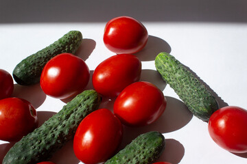 Red fresh tomatos and green cucumber vegetables for summer salade preparation on white background top view 