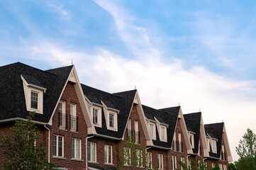 A row of new townhouses with peaked roofs against the blue sky. 