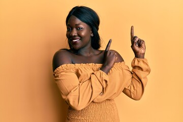 African young woman wearing casual clothes smiling and looking at the camera pointing with two hands and fingers to the side.