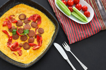 Traditional Delicious omelette with sausage in frying pan, Copy space, Top view, Food Concept, Black Background.