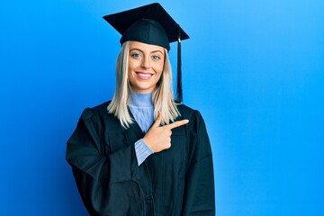 Beautiful blonde woman wearing graduation cap and ceremony robe cheerful with a smile of face...