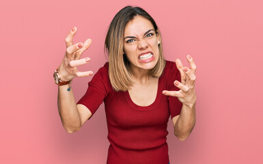 Young blonde girl wearing casual clothes shouting frustrated with rage, hands trying to strangle,...