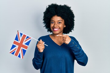 Young african american woman holding united kingdom flag smiling happy pointing with hand and finger
