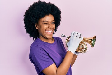 Young african american woman playing trumpet winking looking at the camera with sexy expression,...