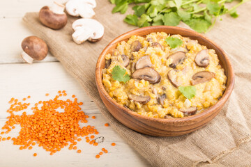 Lentils porridge with champignons. and coriander in a wooden bowl on a white wooden background. Side view, selective focus.