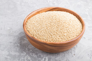 Wooden bowl with raw white quinoa seeds on a gray concrete  background.  Side view.