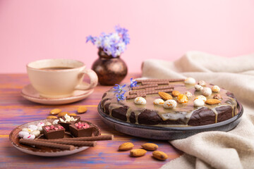 Homemade chocolate brownie cake with caramel cream and almonds with cup of coffee on a colored and pink background. Side view, selective focus.