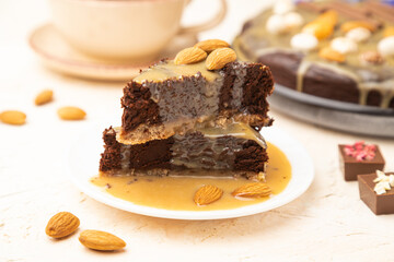 Pieces of chocolate brownie cake with caramel cream and almonds on a white concrete  background. Side view, selective focus.