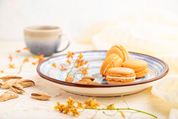 Fototapeta na wymiar Orange macarons or macaroons cakes with cup of coffee on a white concrete background. Side view, selective focus.