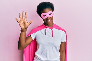 Naklejka premium Young african american girl wearing superhero mask and cape costume showing and pointing up with fingers number five while smiling confident and happy.