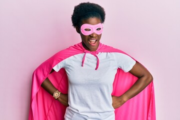 Young african american girl wearing super hero costume and medical mask winking looking at the camera with sexy expression, cheerful and happy face.