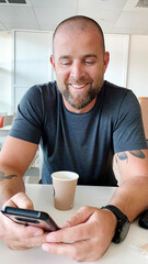 Portrait of the bearded man sitting at the café Drinking Coffee using his phone smiling
