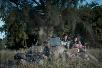 Little brother and sister using laptop doing homework in outdoor public park 