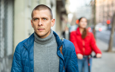 Portrait of handsome serious young man in blue jacket walking autumn street