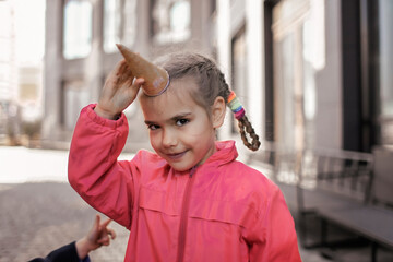 Pretty girl eating ice cream at street over urban background, funny candy girl have fun and hold waffle cone like a horn of unicorn, sweet dessert, street food, outside lifestyle