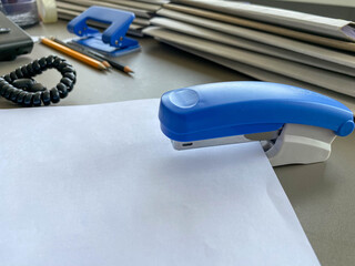A large blue stapler for stapling paper lies next to the folders of documents on the working business desk in the office. Stationery