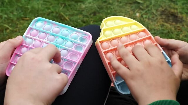 Anonymous children Siblings playing with colorful poppit sensory game. Close up of kid hands Push colorful trendy pop bubble flexible fidget toy. Concentration, antistress, mental issues concept..